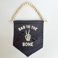 Black banner with 'Bad to the Bone' text and skeleton hand design, hanging from wooden beads.