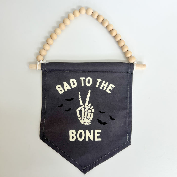 Black banner with 'Bad to the Bone' text and skeleton hand design, hanging from wooden beads.