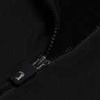 A close-up of the Black - Q-Zip shows a partially unzipped black zipper on smooth, slightly shiny, moisture-wicking fabric. The rectangular pull displays a small white figure icon, possibly swinging a golf club.