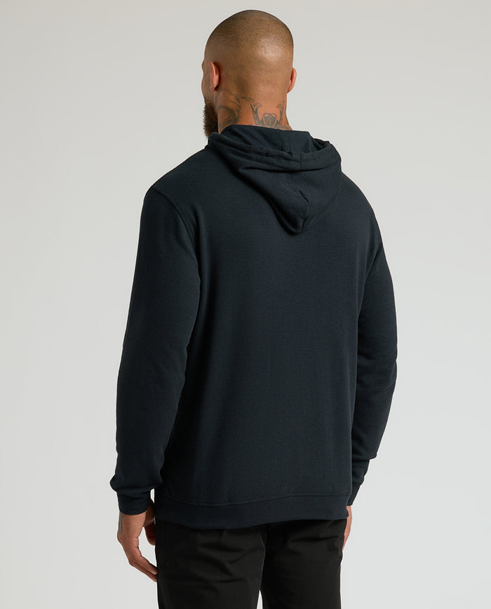 Man wearing All Black Classic Waffle Hoodie, back view, hood down.