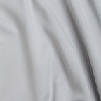 A close-up of Bone - Q-Zip’s light gray fabric shows a smooth, fine weave with gentle folds and a subtle sheen. The athletic fit material features built-in moisture wicking, ensuring all-day comfort.