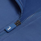 Close-up of the Cooler Blue - Q-Zip’s blue zipper and moisture-wicking fabric. The zipper pull shows a white reclining icon. Visible stitching, textured teeth, and an athletic fit deliver comfort and performance.