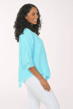 Side shot of a woman wearing a light blue top and white pants on a white background