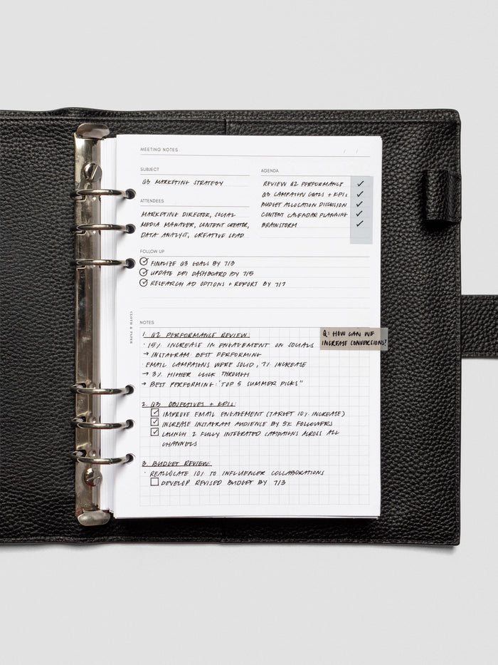 A meeting notes insert neatly filled with handwritten notes, secured in a black leather six-ring planner. The structured layout includes subject, agenda, attendees, follow-up, and a gridded notes section.