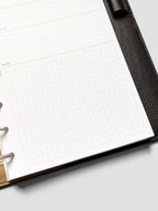 Detail view of a half-letter meeting notes insert inside a black leather planner. The page shows lined sections for follow-up and a large gridded notes area.