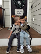 Two children sitting on a step outside a house with a 'First Day of School' sign.