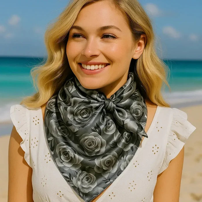 Woman wearing a rose-patterned scarf, smiling, on a beach.