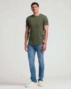 Man wearing an olive green Tall Pima Cotton Blend Curved Hem Crew 4-Pack t-shirt paired with light blue jeans and white sneakers, standing against a plain background.
