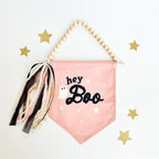 Pink banner with 'hey Boo' text and decorative tassels on a white background with gold stars.