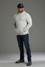 Man wearing a light gray hoodie, dark jeans, and a black cap with a logo on a gray background || light heather gray - 1