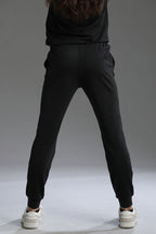 Person wearing black jogger pants and a dark hoodie on a gray background || black