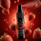A close-up shot of the black intt Deep Throat Strawberry Oral spray bottle emitting a fine, misty spray from its nozzle. The bottle is surrounded by flying fresh strawberries, strawberry pieces, and glossy red droplets against a vibrant red backdrop.