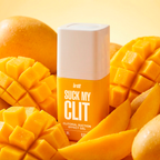 A yellow and white bottle of the intt Suck My Clit clitorial suction gel is nestled closely among a vibrant arrangement of whole, sliced, and cross-hatched cut fresh mangoes.