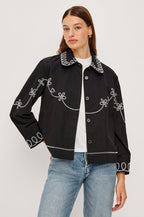 The Keaton is a collared button front jacket with contrast white western inspired embroidery on cuffs, collar, hem, sleeves and bodice in Black colorway. Front view featured on model.