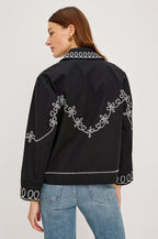 The Keaton is a collared button front jacket with contrast white western inspired embroidery on cuffs, collar, hem, sleeves and bodice in Black colorway. Back view featured on model.