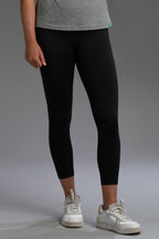 Person wearing black leggings and white sneakers on a gray background || Black Heather