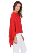A woman wearing a red popover poncho with white pants. Side shot.