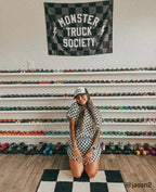 Woman posing in front of a wall of toy monster trucks with a 'Monster Truck Society' flag above.