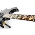 close up image of a guitar against a white background. there is a fret protector on the guitar. It is black with light brown symbols all over it. Every other fret has a brown, black and greenish triangle on it with a white steve vai logo in the center of it. The steve vai logo makes the word "vai" with an upside down triangle, a right side up one, and a line going across the triangles with a curl at the end next to the triangle that is upright.