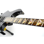 close up image of a guitar against a white background. there is a fret protector on the guitar. It is black with light brown symbols all over it. Every other fret has a brown, black and greenish triangle on it with a white steve vai logo in the center of it. The steve vai logo makes the word "vai" with an upside down triangle, a right side up one, and a line going across the triangles with a curl at the end next to the triangle that is upright.