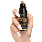 A hand with long white manicured nails holds the 15ml bottle of Orgie Liquid Pulse. The cap is removed to show a black pump dispenser. The small size of the bottle emphasizes its portability and ease of use.