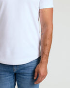 Close-up of a male model wearing a white Pima Cotton Blend Curved Hem Crew 7-Pack shirt paired with blue jeans, showcasing the curved hem detail and comfortable men's basics fit.