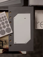 Personal sized grey matte paper dashboard with plastic layer insert into paper slits with other items around it.