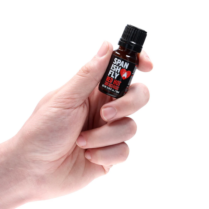 A person's hand is holding the small, dark brown dropper bottle of Spanish Fly Red Hot.
