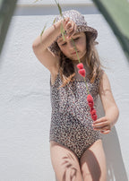 Leopard‑print swimsuit with round leg openings and pink pom‑pom at the straps