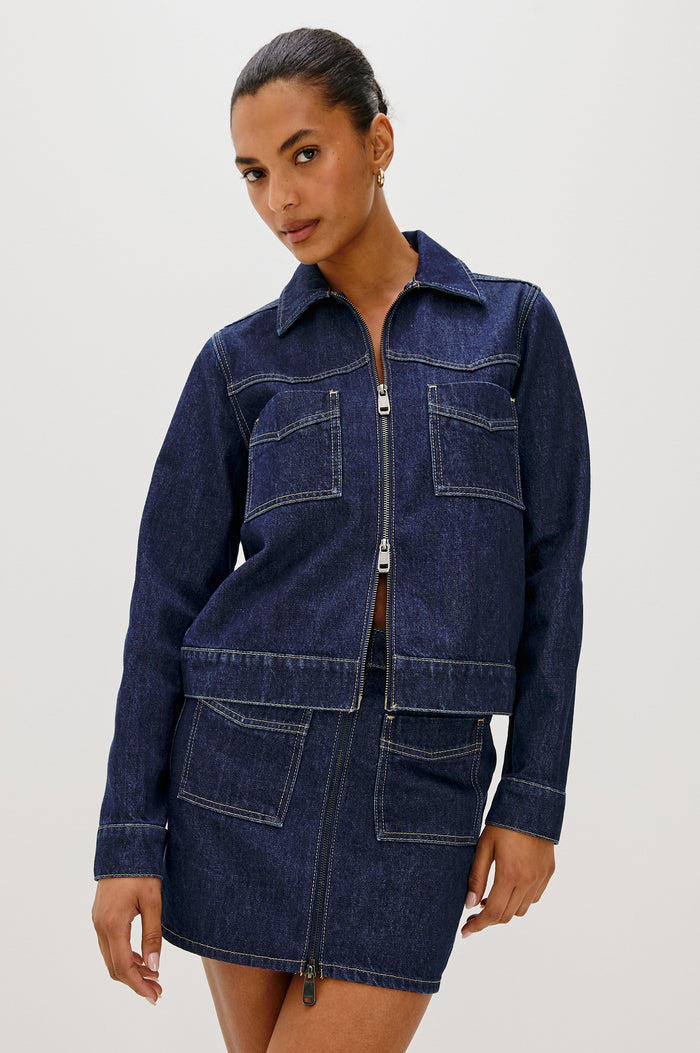 The Trabuco is a collared two-way zip front jacket with two chest pockets and a western style yoke in Deep Indigo colorway - a rinse denim wash. Front view featured on model.