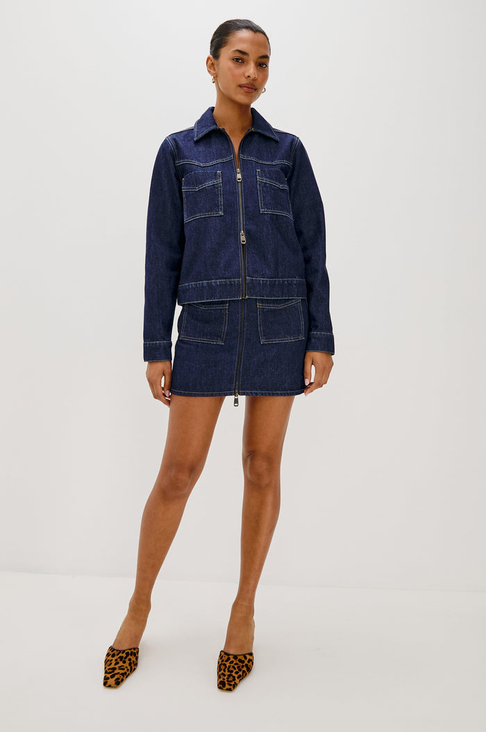 The Trabuco is a collared two-way zip front jacket with two chest pockets and a western style yoke in Deep Indigo colorway - a rinse denim wash. Front full body view featured on model.