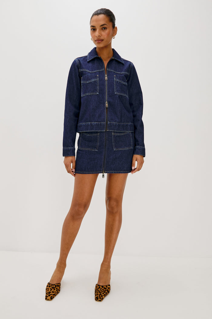 The Trabuco is a collared two-way zip front jacket with two chest pockets and a western style yoke in Deep Indigo colorway - a rinse denim wash. Front full body view featured on model.